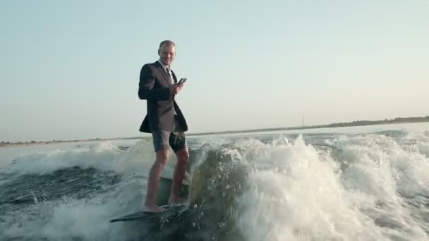 Surfer skaczący na desce w garniturze. Doświadczony wakeboarder spryskuje kamerą krople wody. — Wideo stockowe