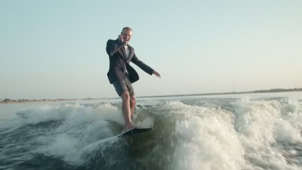 Surfař skákající na wakeboardu v obleku. Surfař mluví po telefonu a jezdí na wakeboardu. Zkušený wakeboarder rozstřikuje do kamery kapky vody. — Stock video