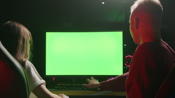 Um cara e uma menina estão sentados em um computador e olhando para uma tela verde — Vídeo de Stock