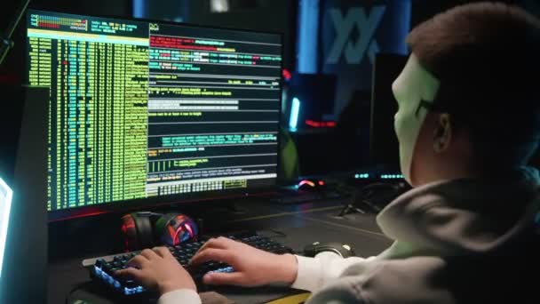 Egy maszkos hacker betör egy adatbázisba egy számítógépen, feltörve egy sötét szobát. — Stock videók