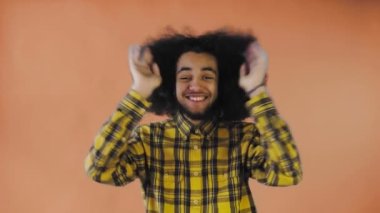 Turuncu arka planda Afro saçlı genç bir adam mutludur. Renkli bir arkaplanda duygular.