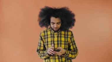 Turuncu arka planda Afrikalı saç stili olan genç bir adam telefonunu çıkardı ama işe yaramadı. Renkli bir arkaplanda duygular