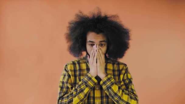 Egy afrikai frizurájú, narancssárga hátterű fiatalember meglepődött. Érzelmek egy színes háttér. — Stock videók