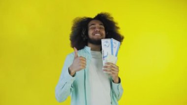 Mutlu bir Afro-Amerikalı adam kameraya bakar, elinde turist makbuzları tutar, sarı bir arka planda tek başına durur.