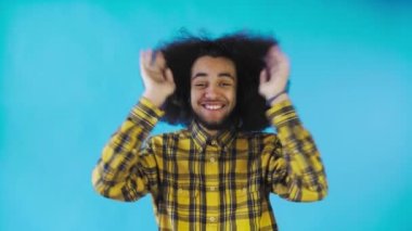 Mavi arka planda Afrikalı saç stili olan genç bir adam mutludur. Renkli bir arkaplanda duygular.