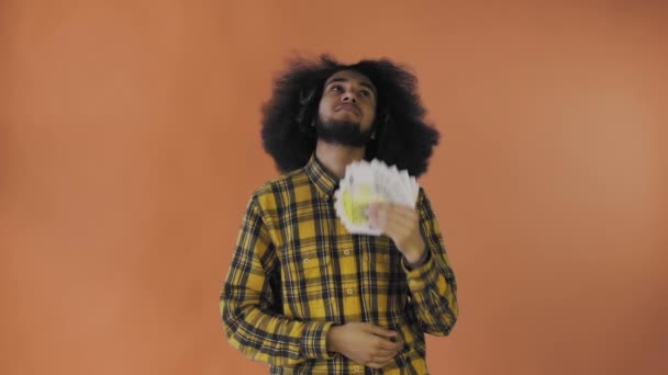 オレンジの背景に隔離されたカメラを見て、幸せアフリカ系アメリカ人の男は彼の手に紙幣のファンを保持します。 — ストック動画