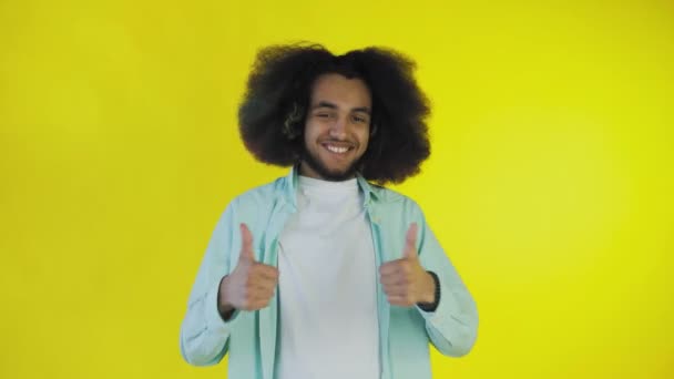 Un hombre afroamericano feliz mirando a la cámara, muestra un parecido con su mano, se encuentra aislado sobre un fondo amarillo — Vídeos de Stock