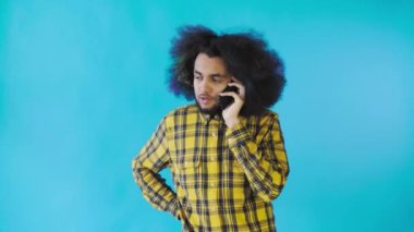 Mavi arka planda Afrikalı saç stili olan genç bir adam telefonda konuşuyor. Renkli bir arkaplanda