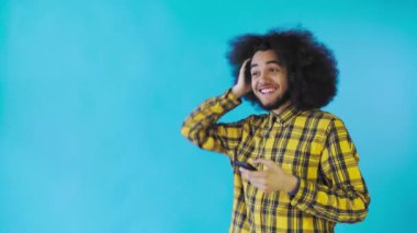Mavi arka planda Afrikalı saç stili olan genç bir adam telefona bakar ve mutlu bir şekilde şaşırır. Renkli bir arkaplanda duygular