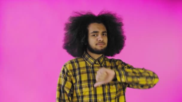 Un uomo afroamericano guarda la telecamera, dà un pollice verso il basso, si trova isolato su uno sfondo rosa — Video Stock