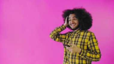 Pembe arka planda Afrikalı saç stili olan genç bir adam telefona bakar ve mutlu bir şekilde şaşırır. Renkli bir arkaplanda duygular