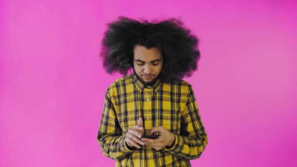 Un giovane con un'acconciatura africana su sfondo rosa tira fuori il telefono, ma non funziona. Emozioni su sfondo colorato — Video Stock
