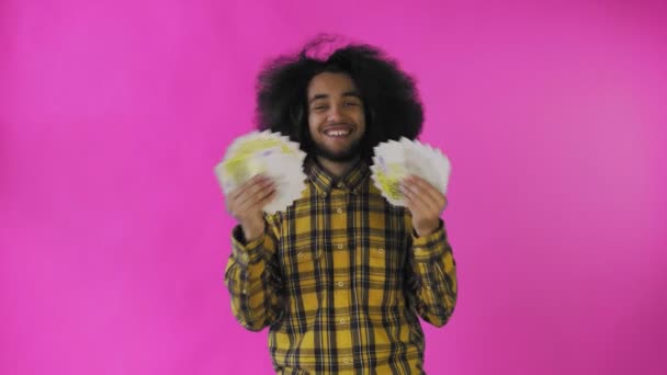 Šťastný Afroameričan, který drží v rukou vějíř bankovek a dívá se do kamery, stojí izolovaně na růžovém pozadí — Stock video