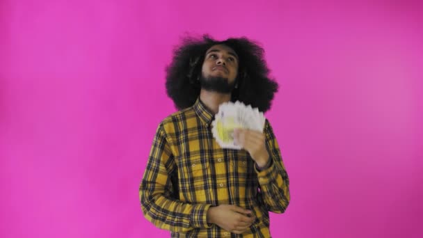 En glad afroamerikansk man som håller ett fan av sedlar i sina händer och tittar på kameran, står isolerad på en rosa bakgrund — Stockvideo