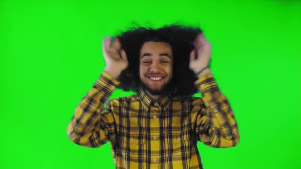 Een jonge man met een Afrikaans kapsel op een groene achtergrond is gelukkig. Emoties op een gekleurde achtergrond. — Stockvideo