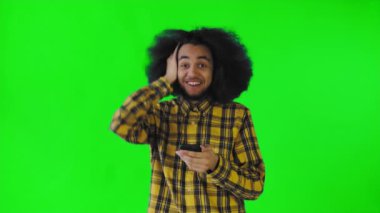 Yeşil arka planda Afrikalı saç stili olan genç bir adam telefona bakar ve mutlu bir şekilde şaşırır. Renkli bir arkaplanda duygular