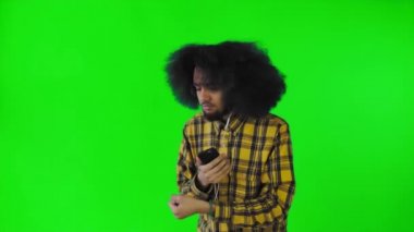 Yeşil arka planda Afrikalı saç stili olan genç bir adam müzik ve kulaklık dinliyor. Renkli bir arkaplanda