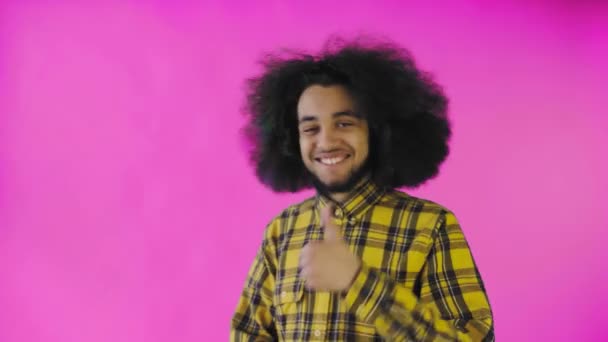Šťastný afroameričan se dívá do kamery, ukazuje něco jako rukou, stojí izolovaný na růžovém pozadí — Stock video