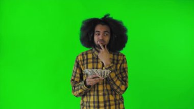 Elinde para tutan ve neye harcayacağını düşünen mutlu bir Afro-Amerikalı yeşil bir arka planda tek başına duruyor.