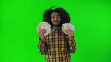 Elinde banknot yelpazesi olan mutlu bir Afro-Amerikalı adam yeşil bir arka planda tek başına kameraya bakıyor.