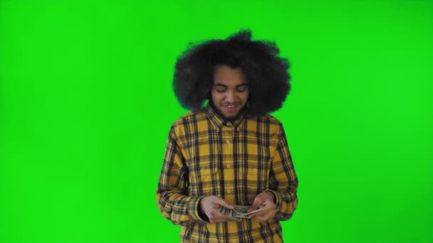 Un homme afro-américain heureux tenant des billets dans ses mains, les comptant et regardant la caméra, debout isolé sur un fond vert — Video