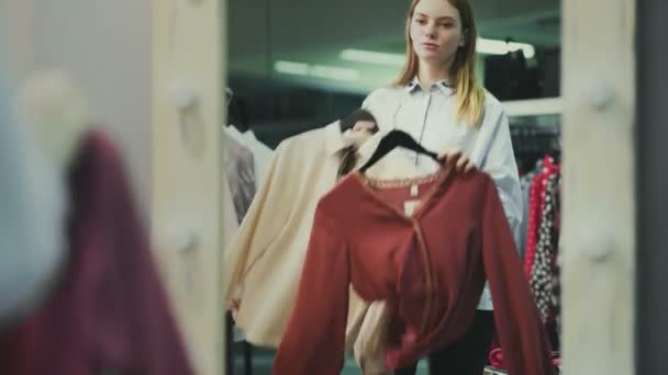 Een mooi meisje past kleren in de paskamer in een kledingwinkel. Winkelen — Stockvideo