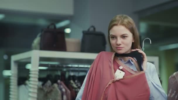 Een mooi meisje past kleren in een kledingwinkel. Winkelen — Stockvideo