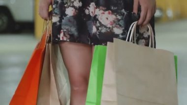 Elbise giymiş, elinde alışveriş torbalarıyla şık genç bir bayanın bacaklarına yakın çekim.
