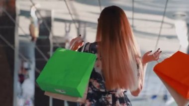 Elbiseli, şık ve genç bir Asyalı müşterinin yakın çekimi ve ellerinde alışveriş torbalarıyla kendi etrafında dönüyor.