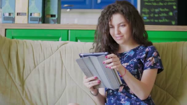 Een jonge vrouw met een tablet zit op de bank en surft op het web. — Stockvideo