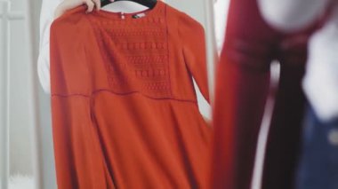 Genç bir kadın elbise deniyor ve ne giyeceğine karar veremiyor, kızıyor ve elbiselerini yere atıyor. Tanımlanamayan bir kızın yakın çekimi.