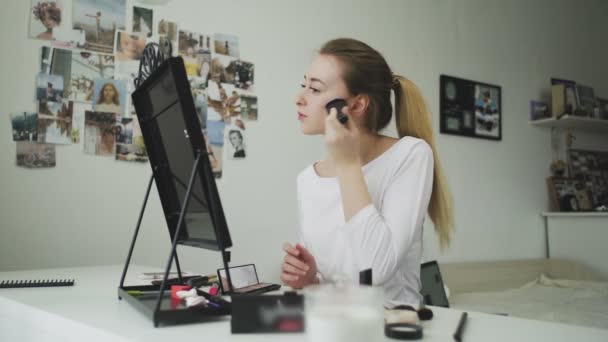 Une jeune femme se maquille assise à une table devant un miroir — Video