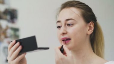 Kız dudaklarını rujla boyuyor. Yüze yakın çekim. Ruj süren bir kadının makro fotoğrafı. Yüz makrosu. Kız küçük bir aynaya bakıyor.