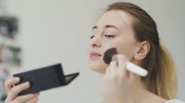 Genç bir kadın küçük bir aynaya bakarken makyajını yapıyor.