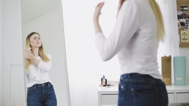 Una mujer descontenta de pie frente a un espejo mira su cuerpo. Complejos de apariencia y cuerpo — Vídeos de Stock