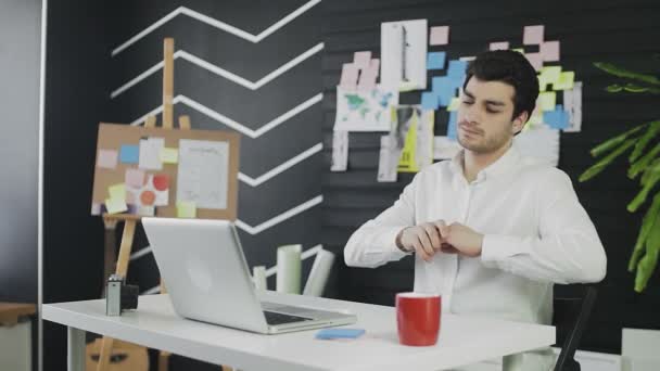 Mladý muž bělošského vzhledu sedí u počítače a pracuje na dálku. Mladý muž se zahřeje na židli a pokračuje v práci. — Stock video
