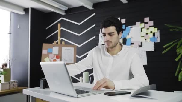 En ung mand af kaukasisk udseende tænder computeren og begynder at arbejde. Fjernarbejde. Freelance. Video i bevægelse – Stock-video