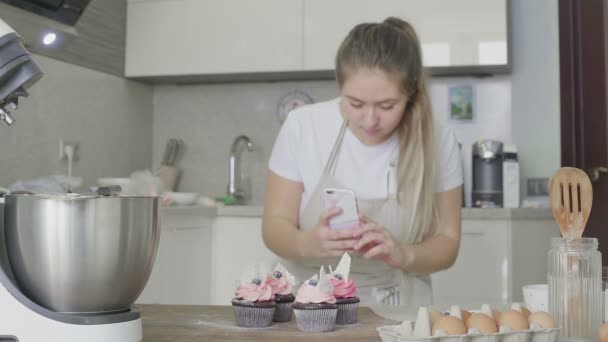 Krásná dívka v kuchyni fotí připravené dortíky na svém telefonu. Ruční práce — Stock video