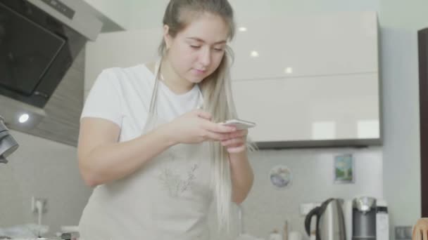 A beautiful girl in the kitchen takes pictures of prepared cupcakes on her phone. Handmade work — Stock Video