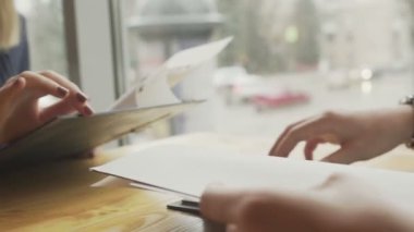 Bir erkek ve bir kadın menüden bir yemek seçiyorlar, pencerenin yanındaki bir kafede karşılıklı oturuyorlar. Hoş bir çiftin randevusu var. Kapat.