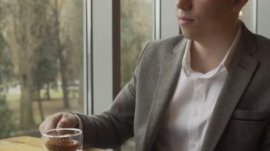 Bir iş adamı pencerenin yanında oturur, yeşil çaylı bir bardak kaldırır ve içer.