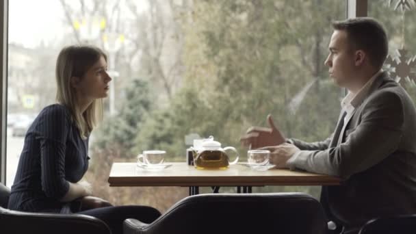 Een man en een vrouw zitten tegenover elkaar in een café of restaurant bij het raam en communiceren. Een afspraakje in een café of restaurant. Romantische sfeer — Stockvideo