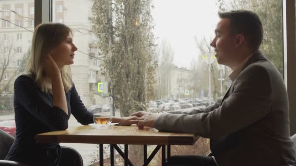En man och en kvinna sitter mittemot varandra i ett café eller restaurang vid fönstret och kommunicerar. En dejt på ett café eller restaurang. Romantisk atmosfär — Stockvideo