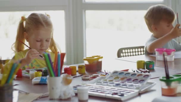 Anak-anak duduk di meja dan menggambar di atas kertas dengan warna dan kuas yang berbeda — Stok Video