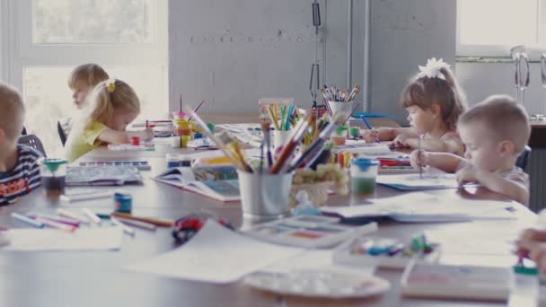 Çocuklar masaya oturur ve farklı renkler ve fırçalarla kağıda resim çizerler. — Stok video