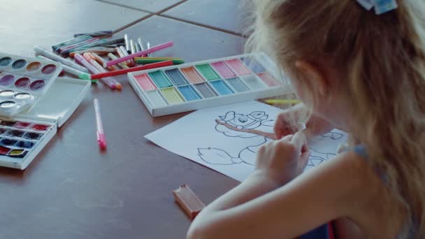 Egy kislány ül az asztalnál és rajzol különböző színekkel és ecsetekkel. — Stock videók