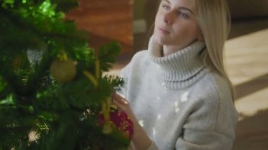 Süveter giyen genç ve güzel bir sarışın Noel ağacının yanında oturuyor ve bir Noel balosu düzenliyor. Evin penceresinin yanında altında hediyeler olan bir Noel ağacı..