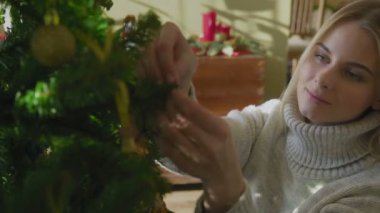 Süveter giyen genç ve güzel bir sarışın Noel ağacının yanında oturuyor ve bir Noel balosu düzenliyor. Evin penceresinin yanında altında hediyeler olan bir Noel ağacı..