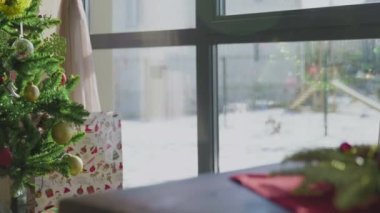 İki kırmızı mum ve bir altın mumu olan ebedi yeşil bir çelenk. Arka planda süslü bir Noel ağacı var. Noel arifesinde Hıristiyanların gelenek ve adetleri.