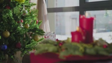 İki kırmızı mum ve bir altın mumu olan ebedi yeşil bir çelenk. Arka planda süslü bir Noel ağacı var. Noel arifesinde Hıristiyanların gelenek ve adetleri.